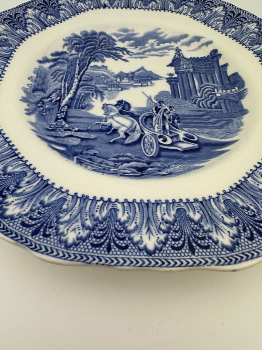 An octagonal-edged blue and white transferware plate featuring a central classical chariot scene surrounded by an ornate feather-patterned border. View IV