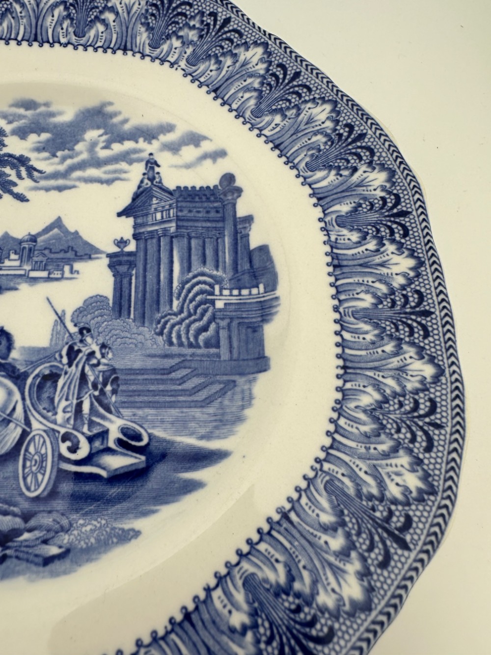 An octagonal-edged blue and white transferware plate featuring a central classical chariot scene surrounded by an ornate feather-patterned border. View V