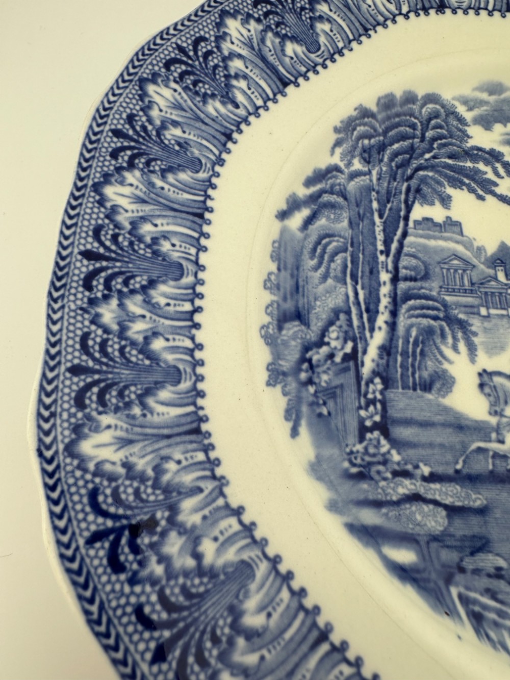 An octagonal-edged blue and white transferware plate featuring a central classical chariot scene surrounded by an ornate feather-patterned border. View VI