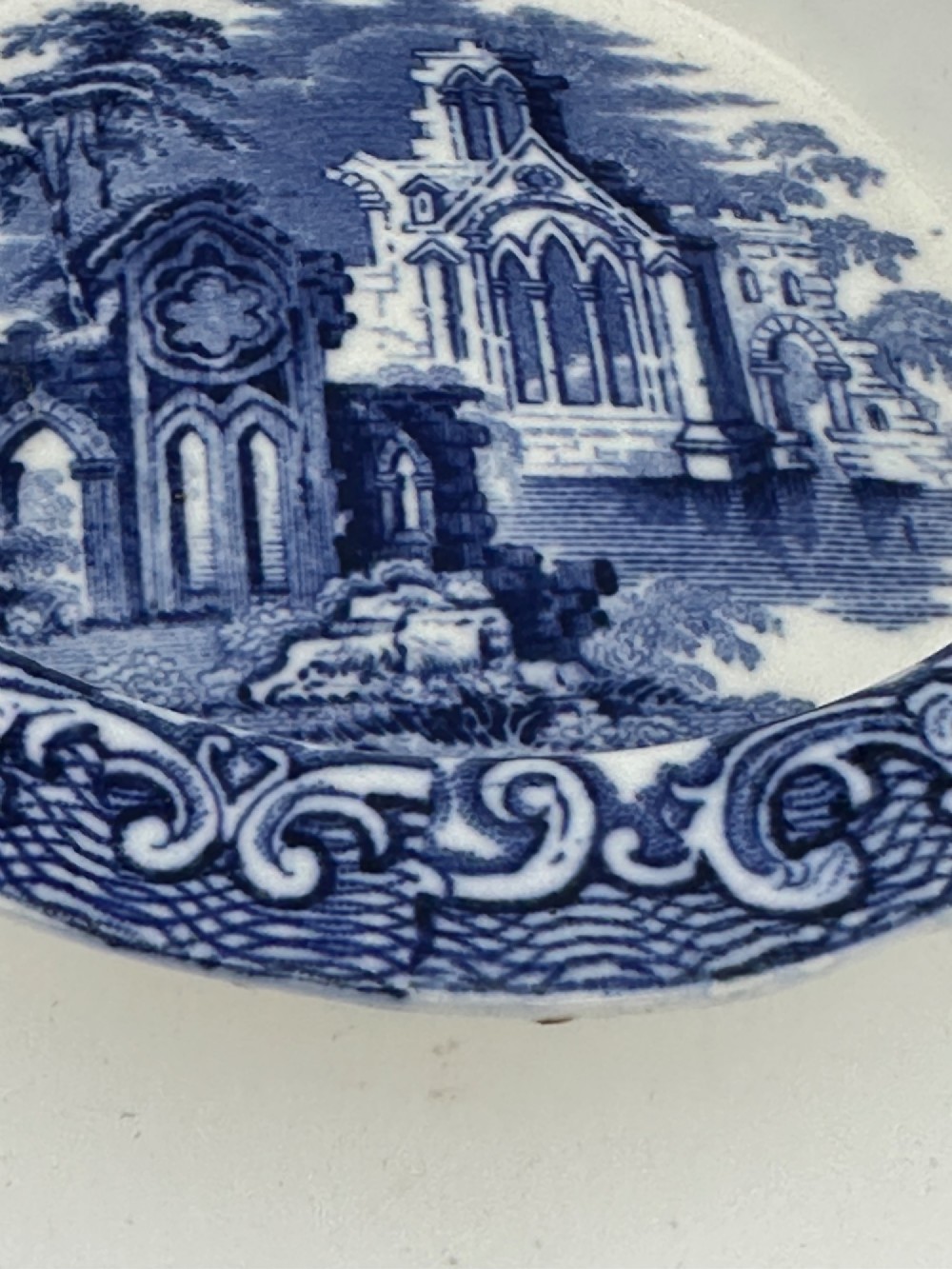 A circular blue and white transferware ceramic dish featuring a central printed depiction of abbey ruins framed by a decorative scrolled border. View VI