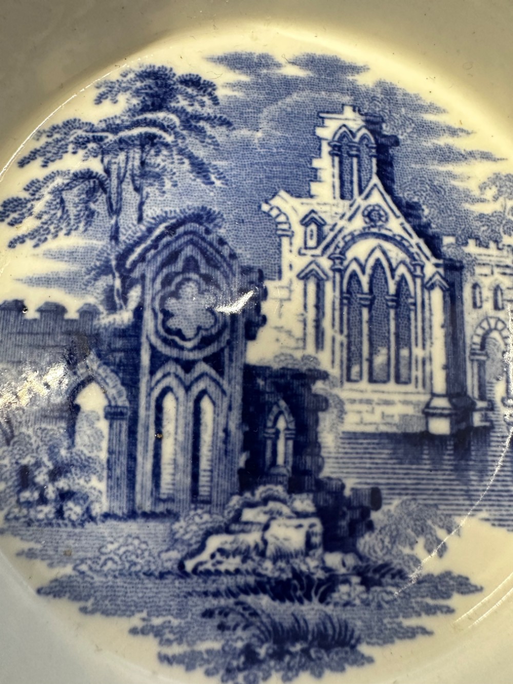 A circular blue and white transferware ceramic dish featuring a central printed depiction of abbey ruins framed by a decorative scrolled border. View IX