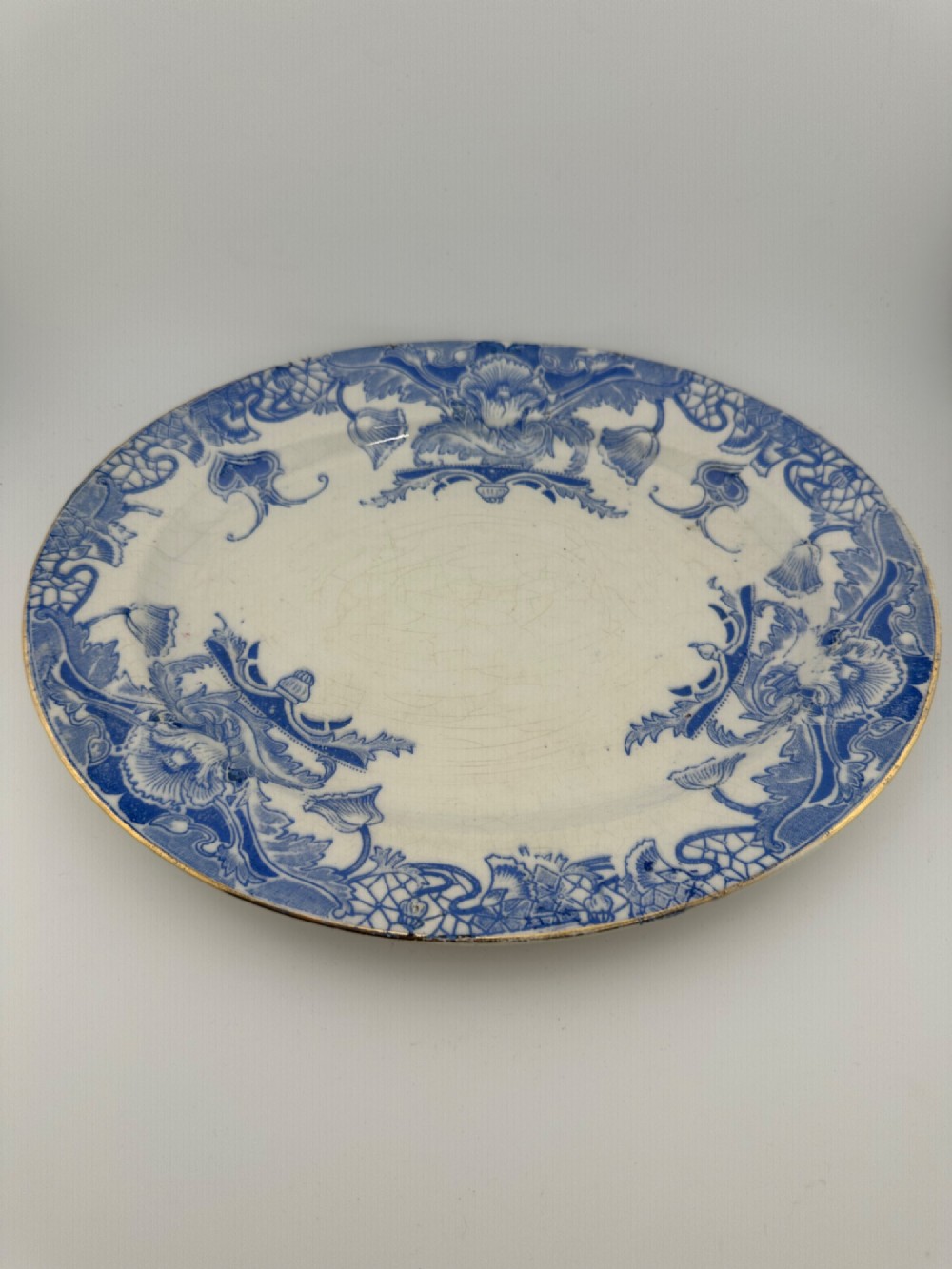 An early Victorian oval earthenware platter featuring a pale blue floral transferware border pattern and a gilded outer rim. View II