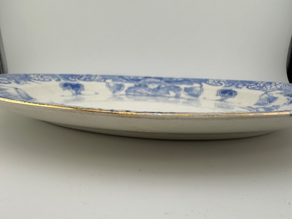 An early Victorian oval earthenware platter featuring a pale blue floral transferware border pattern and a gilded outer rim. View V
