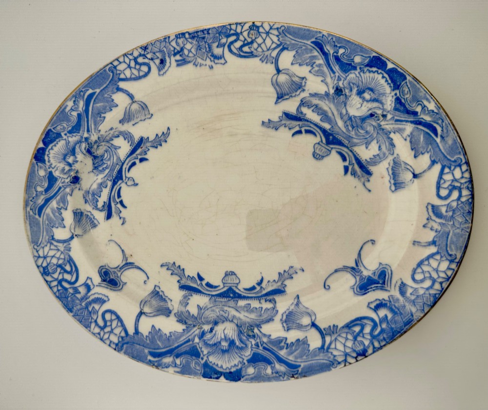 An early Victorian oval earthenware platter featuring a pale blue floral transferware border pattern and a gilded outer rim.