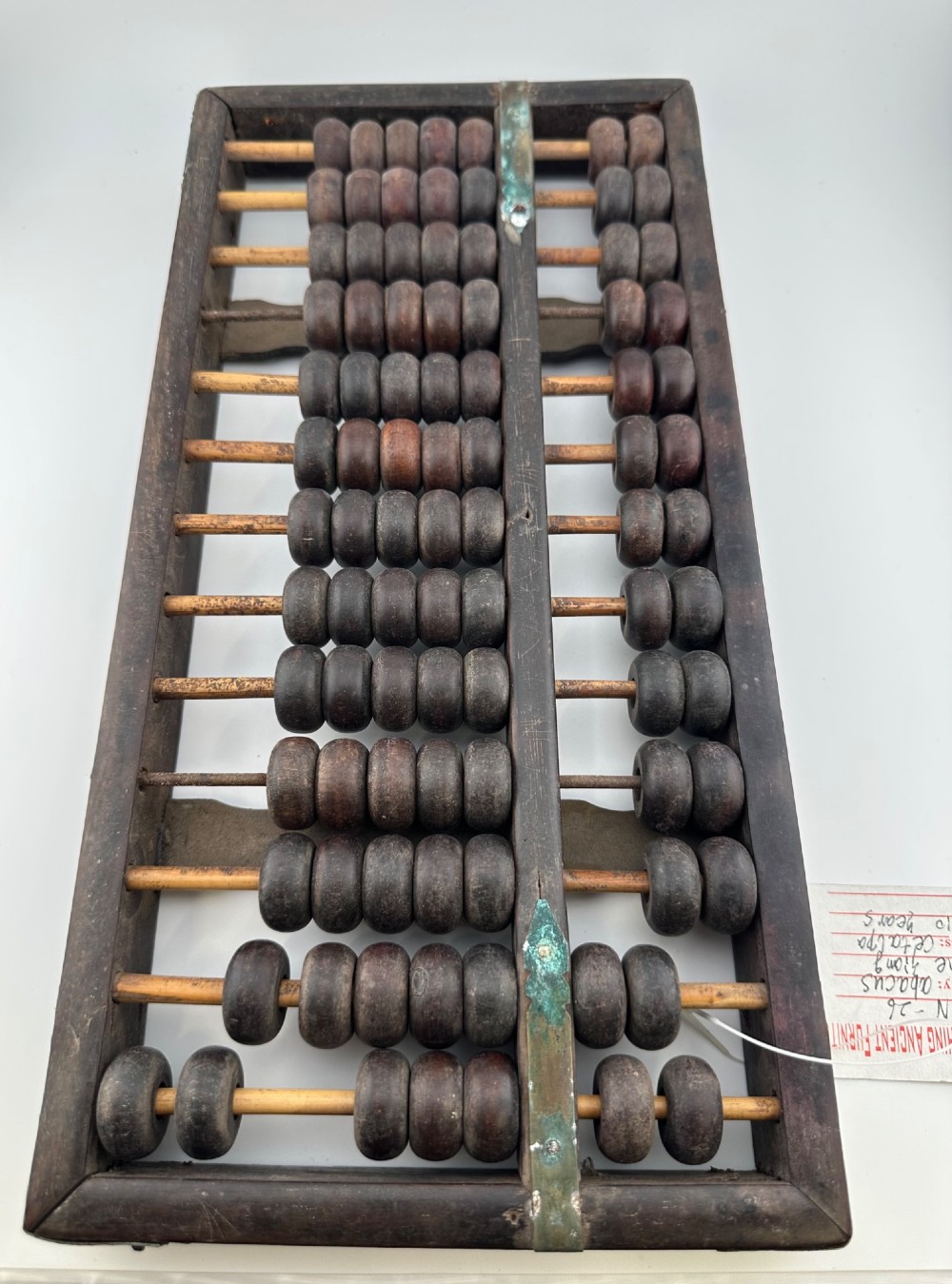 A rectangular dark hardwood Chinese suanpan abacus with two upper beads and five lower beads per rod, reinforced with oxidised brass plates.
