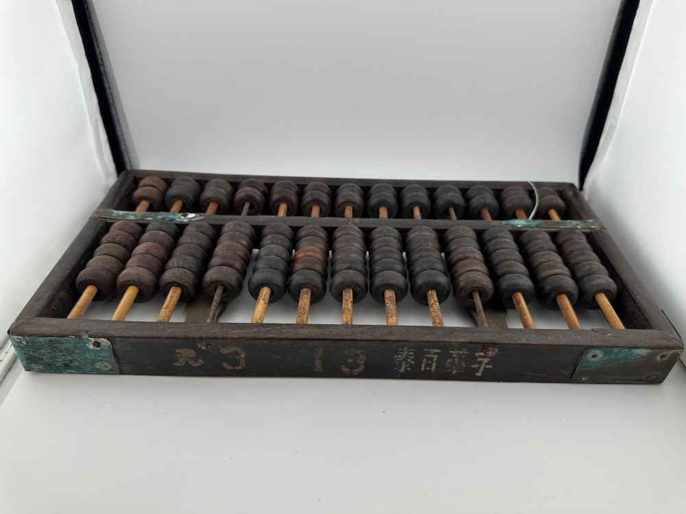 A rectangular dark hardwood Chinese suanpan abacus with two upper beads and five lower beads per rod, reinforced with oxidised brass plates. View III