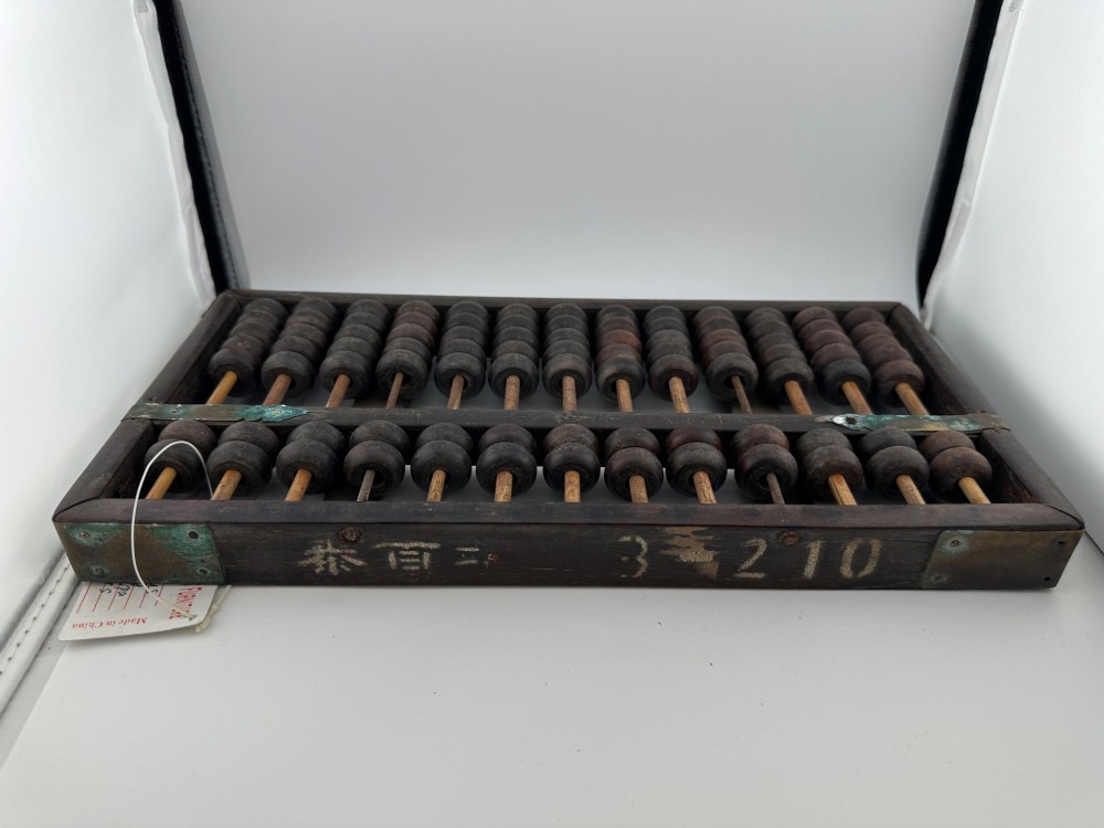 A rectangular dark hardwood Chinese suanpan abacus with two upper beads and five lower beads per rod, reinforced with oxidised brass plates. View IV