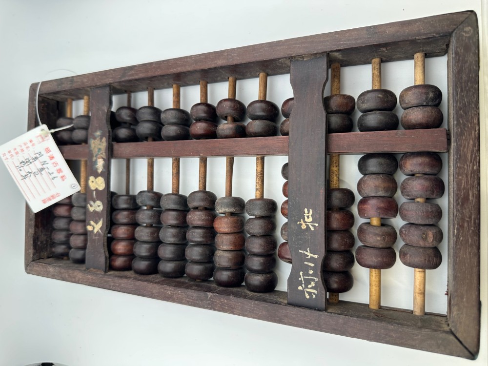A rectangular dark hardwood Chinese suanpan abacus with two upper beads and five lower beads per rod, reinforced with oxidised brass plates. View V