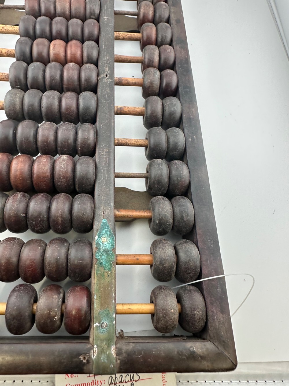 A rectangular dark hardwood Chinese suanpan abacus with two upper beads and five lower beads per rod, reinforced with oxidised brass plates. View X