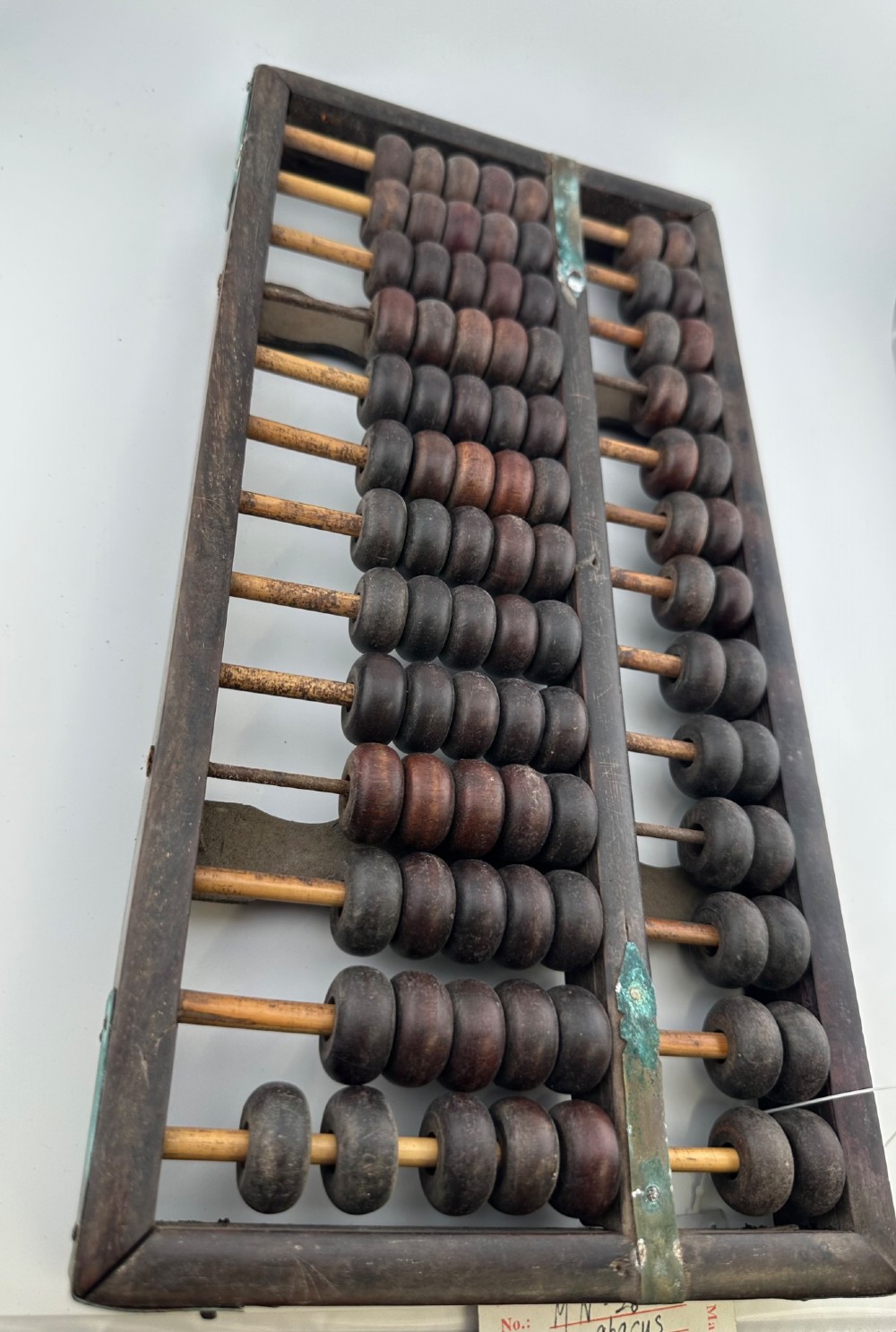 A rectangular dark hardwood Chinese suanpan abacus with two upper beads and five lower beads per rod, reinforced with oxidised brass plates. View XI