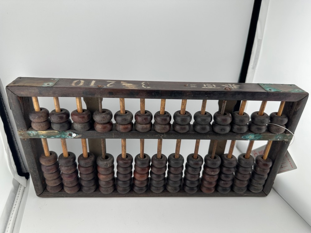 A rectangular dark hardwood Chinese suanpan abacus with two upper beads and five lower beads per rod, reinforced with oxidised brass plates. View XII
