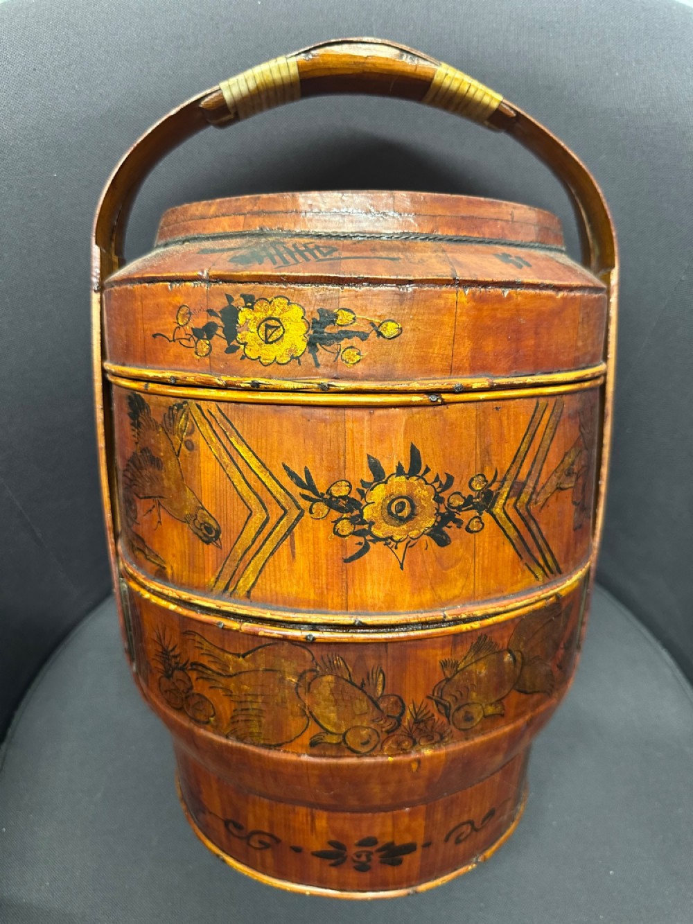 A three-tiered late 19th-century Chinese bamboo and wood food carrier with an arched handle, featuring hand-painted yellow flowers, birds, and goldfish against a warm brown lacquer finish.