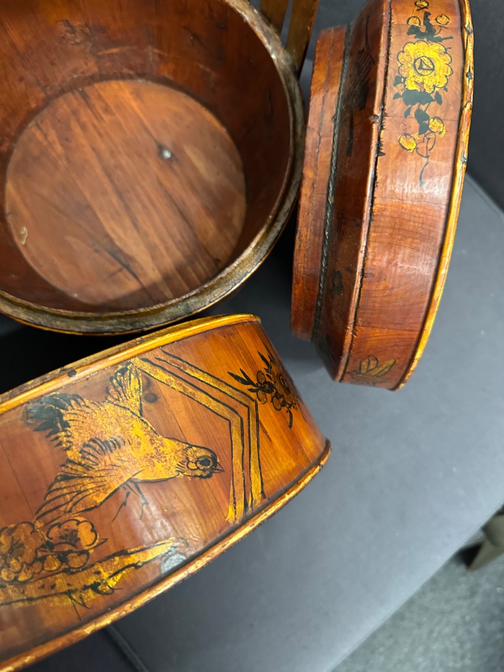 A three-tiered late 19th-century Chinese bamboo and wood food carrier with an arched handle, featuring hand-painted yellow flowers, birds, and goldfish against a warm brown lacquer finish. View XIII