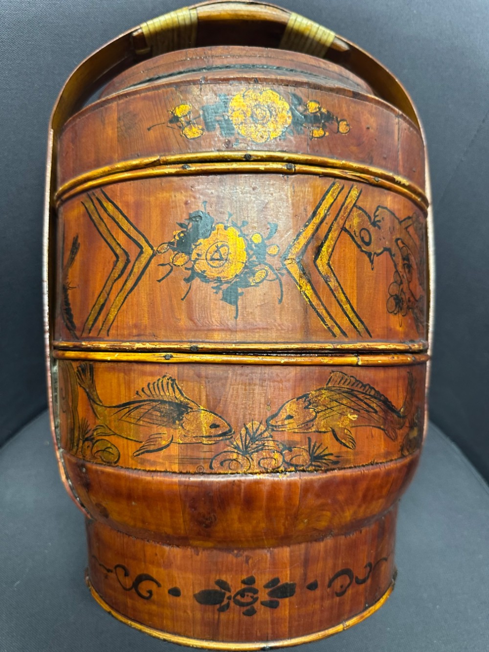 A three-tiered late 19th-century Chinese bamboo and wood food carrier with an arched handle, featuring hand-painted yellow flowers, birds, and goldfish against a warm brown lacquer finish. View XIV