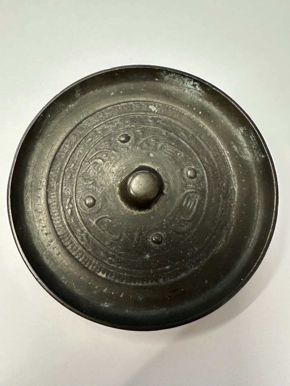 A circular ancient bronze mirror back featuring a prominent central knob, raised concentric circular borders, and stylized dragon motifs in low relief.