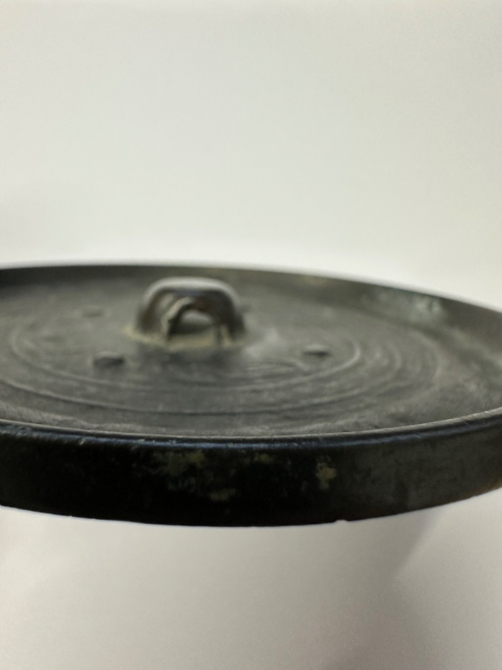 A circular ancient bronze mirror back featuring a prominent central knob, raised concentric circular borders, and stylized dragon motifs in low relief. View II