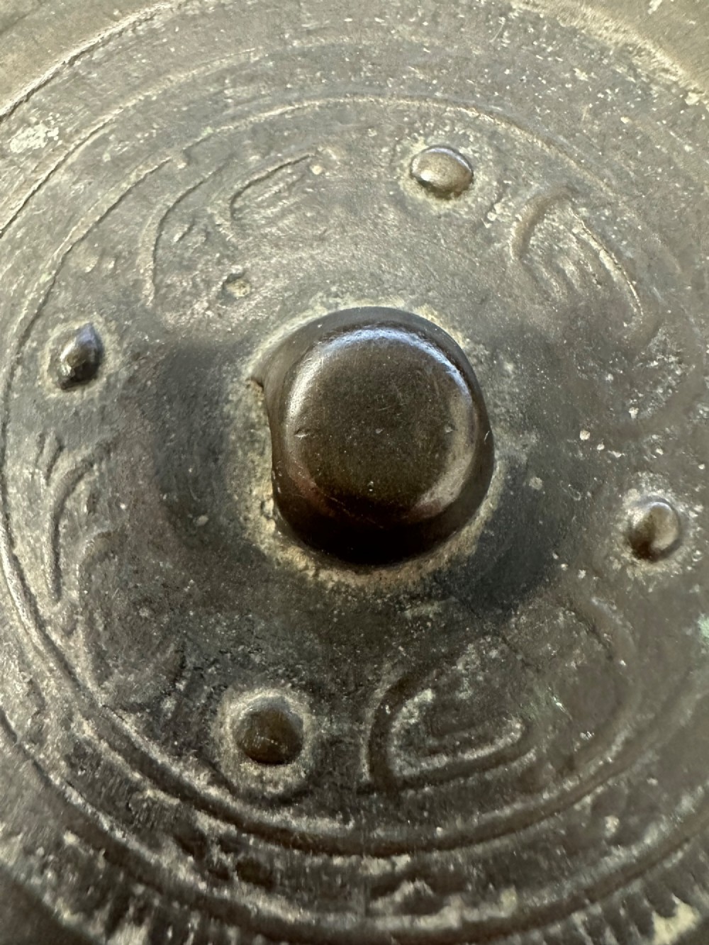 A circular ancient bronze mirror back featuring a prominent central knob, raised concentric circular borders, and stylized dragon motifs in low relief. View VI