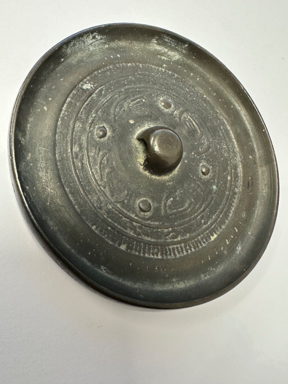 A circular ancient bronze mirror back featuring a prominent central knob, raised concentric circular borders, and stylized dragon motifs in low relief. View VII