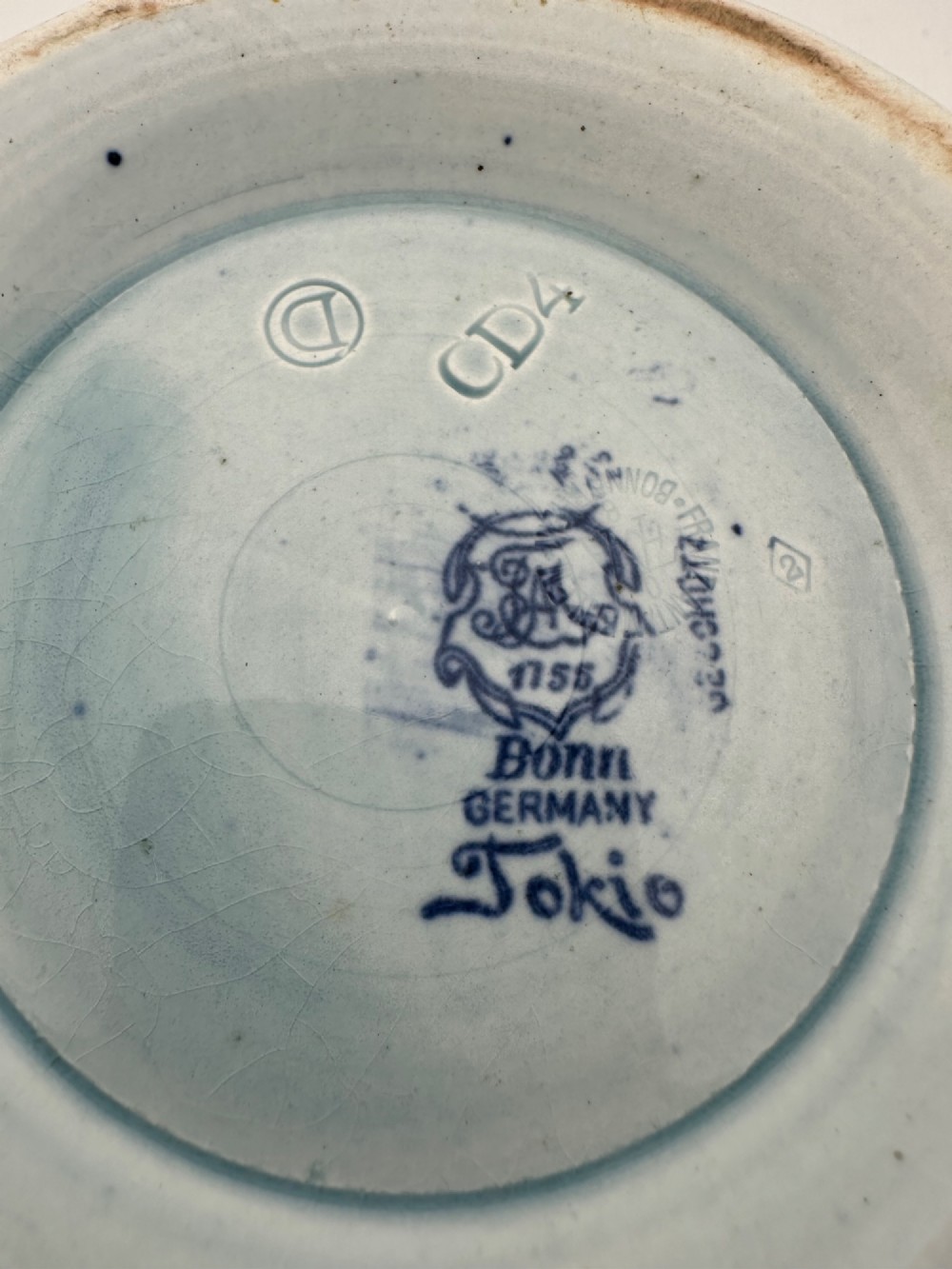 A deep circular footed earthenware bowl decorated with blue and white floral and landscape transferware patterns with a brown rim. View III