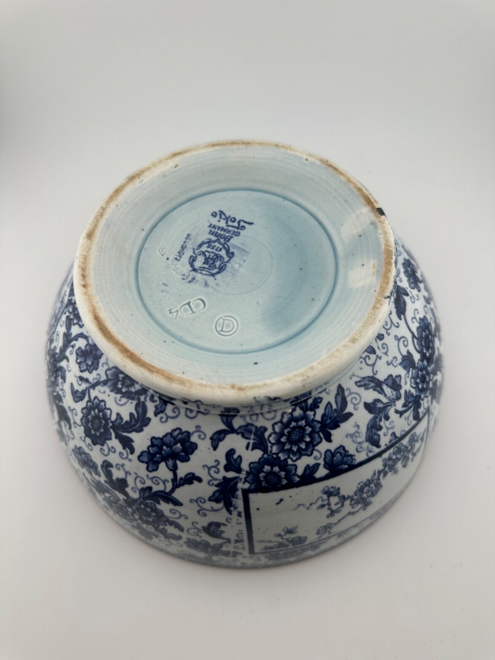 A deep circular footed earthenware bowl decorated with blue and white floral and landscape transferware patterns with a brown rim. View VII