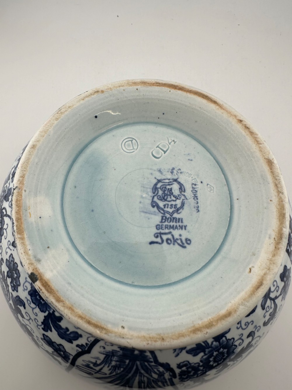 A deep circular footed earthenware bowl decorated with blue and white floral and landscape transferware patterns with a brown rim. View VIII