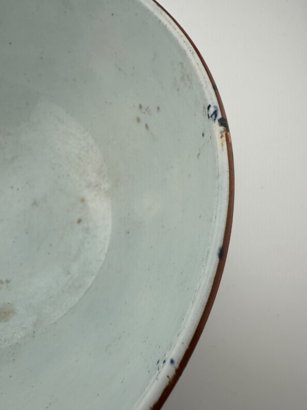 A deep circular footed earthenware bowl decorated with blue and white floral and landscape transferware patterns with a brown rim. View XI