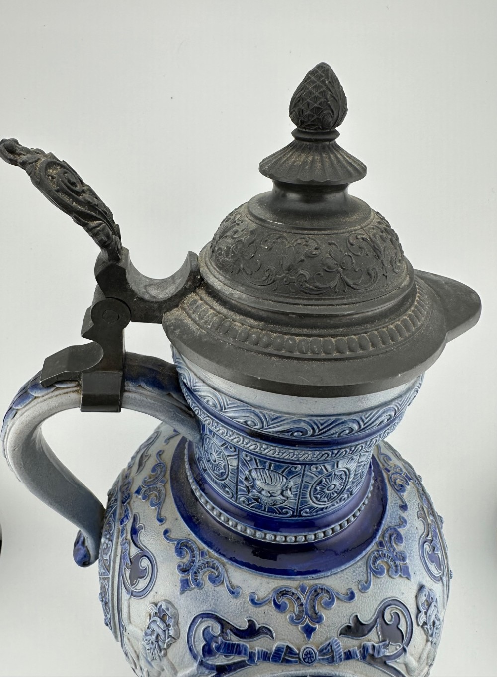 A blue and grey salt-glazed stoneware jug featuring relief-moulded geometric patterns, mask motifs, and a hinged pewter lid. View III