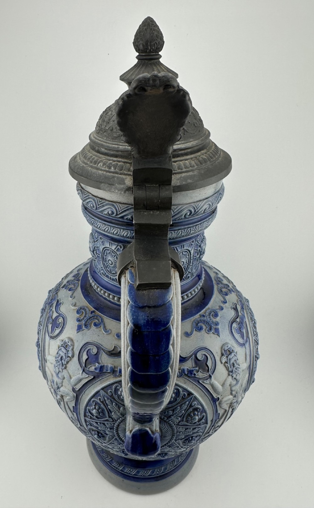 A blue and grey salt-glazed stoneware jug featuring relief-moulded geometric patterns, mask motifs, and a hinged pewter lid. View IV