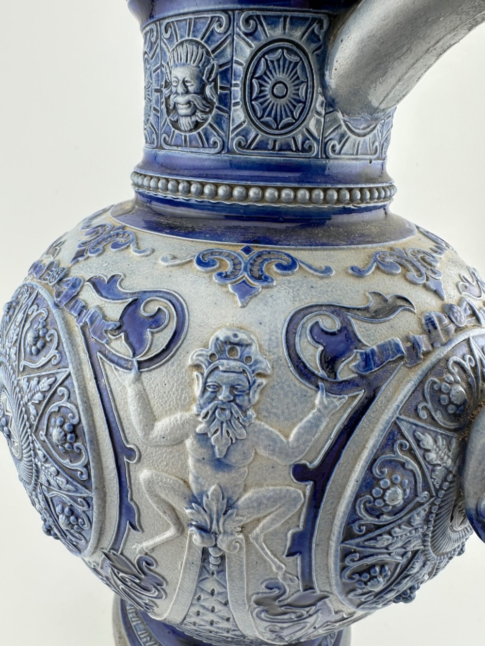 A blue and grey salt-glazed stoneware jug featuring relief-moulded geometric patterns, mask motifs, and a hinged pewter lid. View V