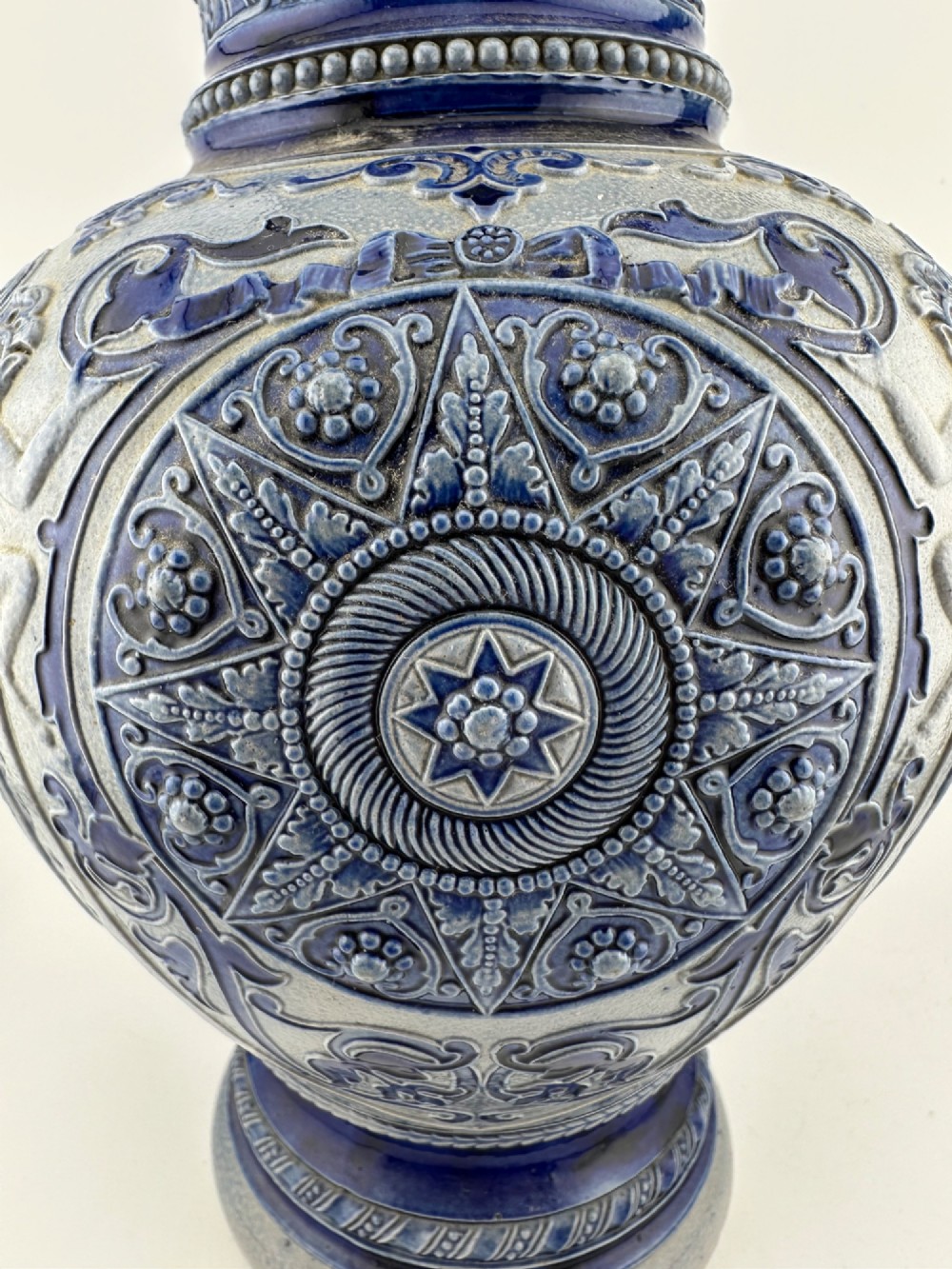 A blue and grey salt-glazed stoneware jug featuring relief-moulded geometric patterns, mask motifs, and a hinged pewter lid. View VII