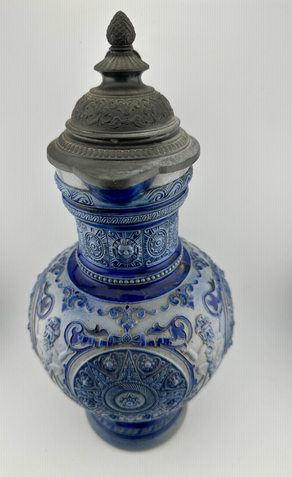 A blue and grey salt-glazed stoneware jug featuring relief-moulded geometric patterns, mask motifs, and a hinged pewter lid. View IX