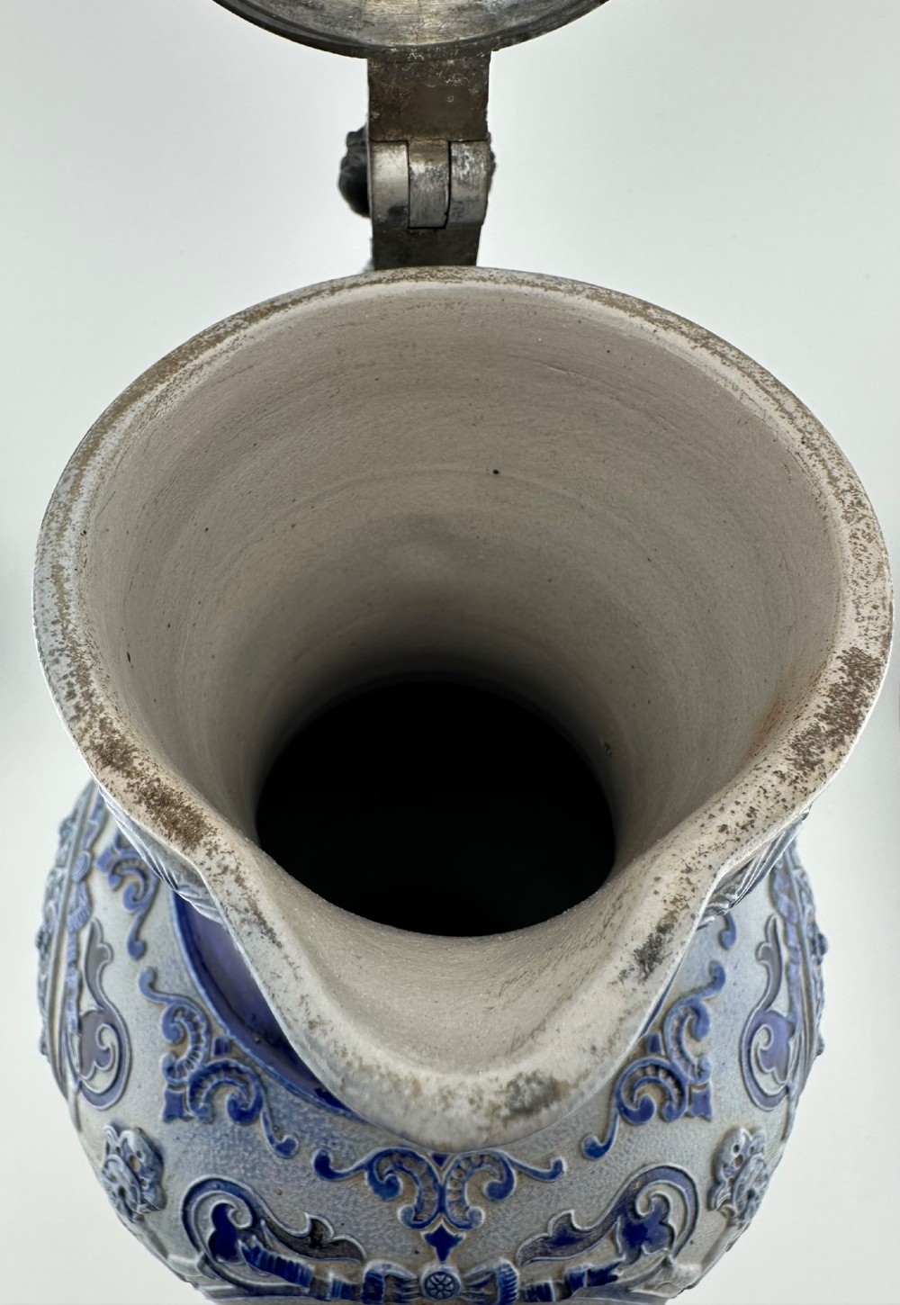 A blue and grey salt-glazed stoneware jug featuring relief-moulded geometric patterns, mask motifs, and a hinged pewter lid. View X