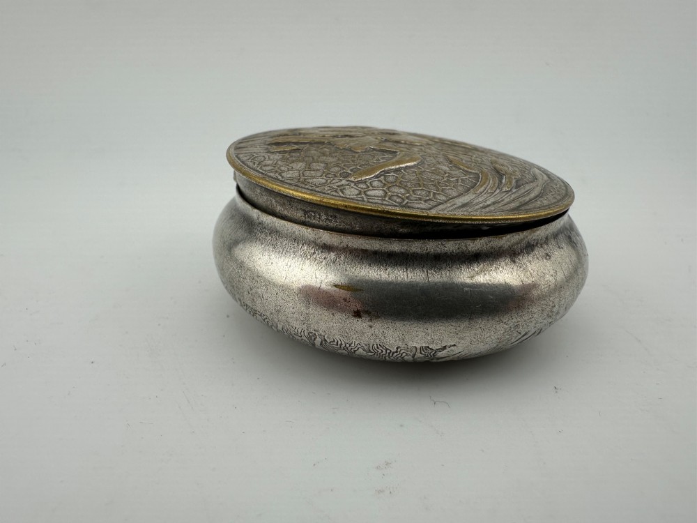 A circular antique Art Nouveau white metal compact box featuring a relief-carved iris floral design with brass highlights and a textured background. View IX