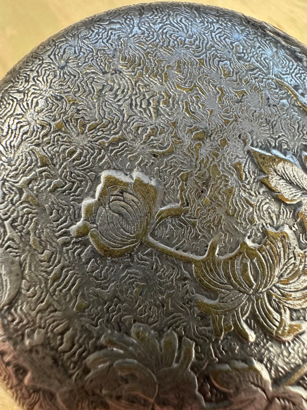 A circular antique Art Nouveau white metal compact box featuring a relief-carved iris floral design with brass highlights and a textured background. View XIII