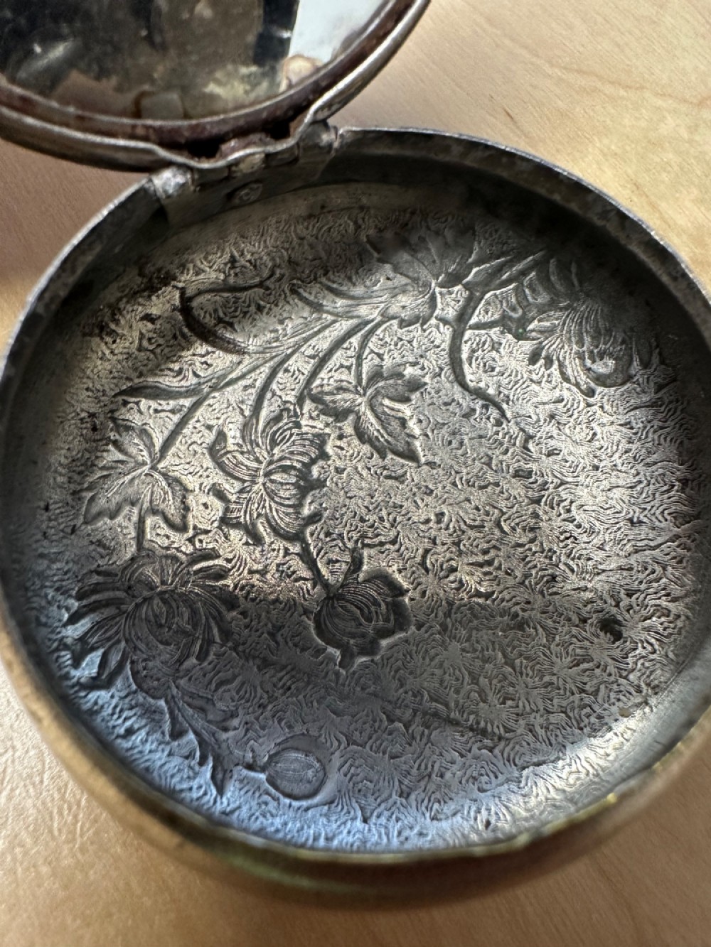 A circular antique Art Nouveau white metal compact box featuring a relief-carved iris floral design with brass highlights and a textured background. View XIV