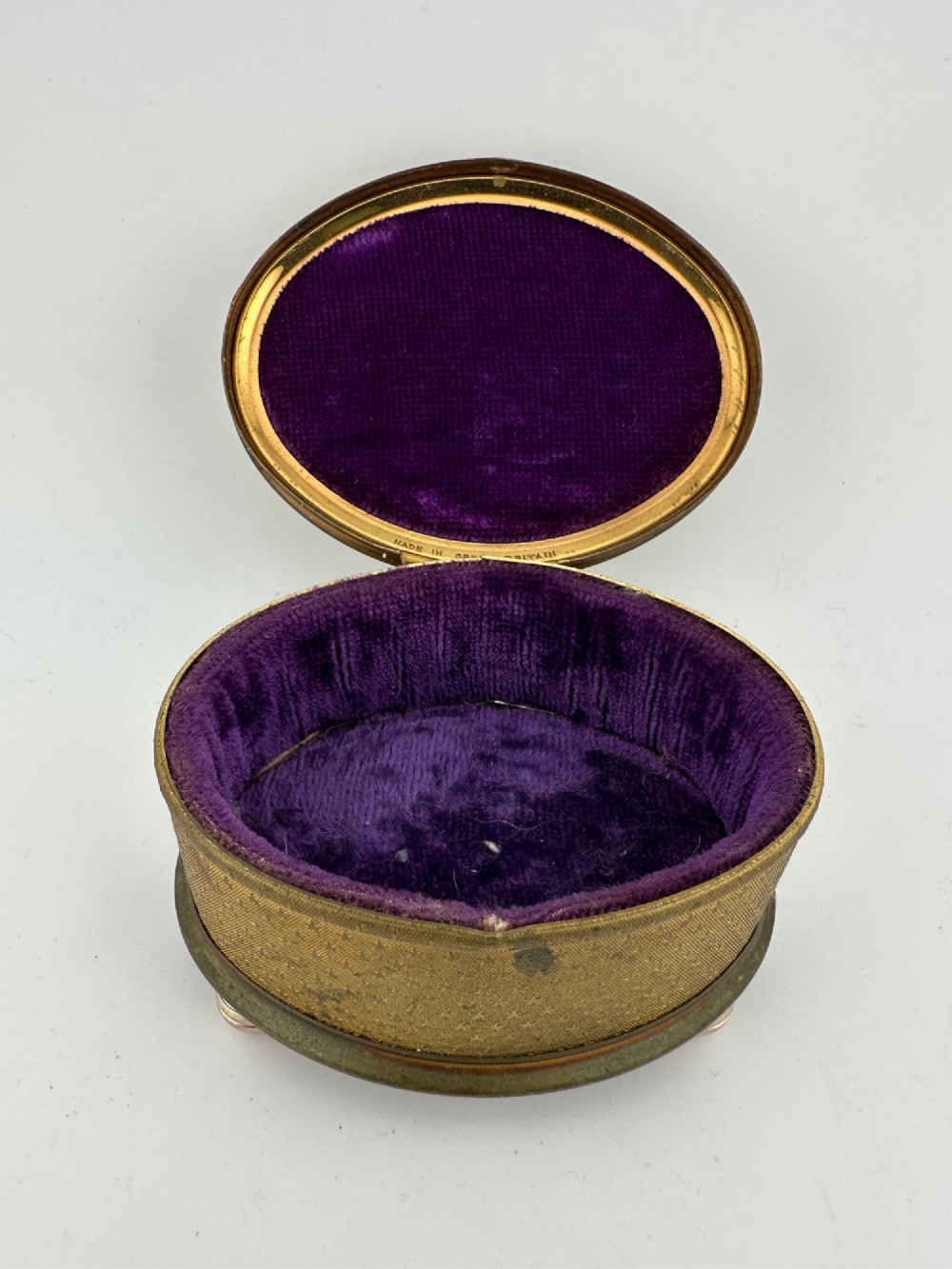 An oval vintage metal trinket box featuring a printed floral motif on the lid, star-patterned side panels, small rounded feet, and a velvet lining. View II