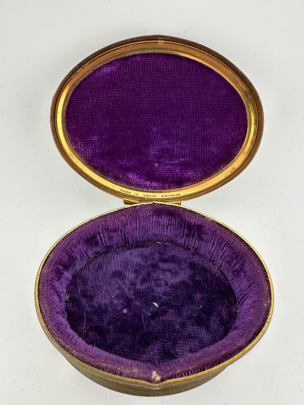 An oval vintage metal trinket box featuring a printed floral motif on the lid, star-patterned side panels, small rounded feet, and a velvet lining. View III