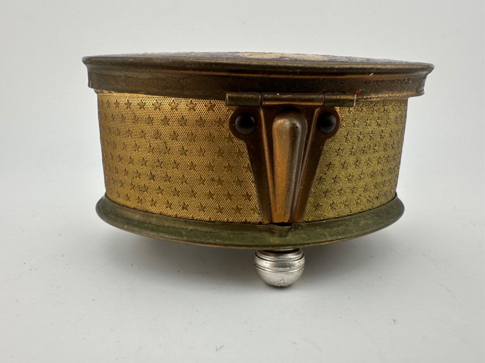 An oval vintage metal trinket box featuring a printed floral motif on the lid, star-patterned side panels, small rounded feet, and a velvet lining. View VII
