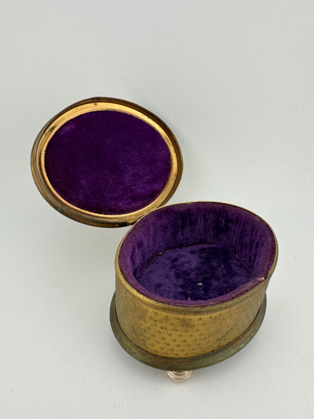 An oval vintage metal trinket box featuring a printed floral motif on the lid, star-patterned side panels, small rounded feet, and a velvet lining. View X