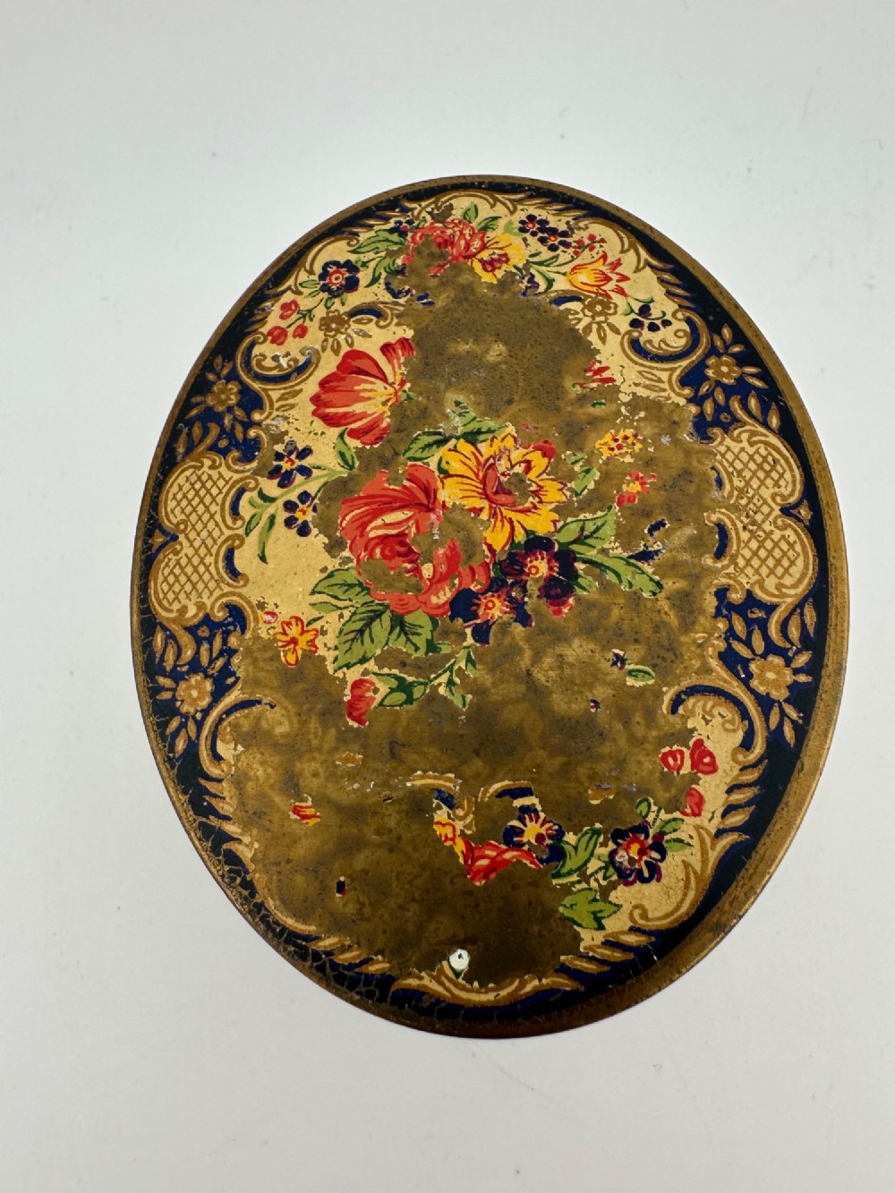 An oval vintage metal trinket box featuring a printed floral motif on the lid, star-patterned side panels, small rounded feet, and a velvet lining. View XI