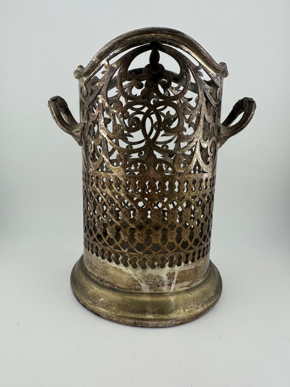 An antique silver-plated cylindrical wine bottle holder featuring pierced scroll fretwork, two side handles, and a flared circular base.