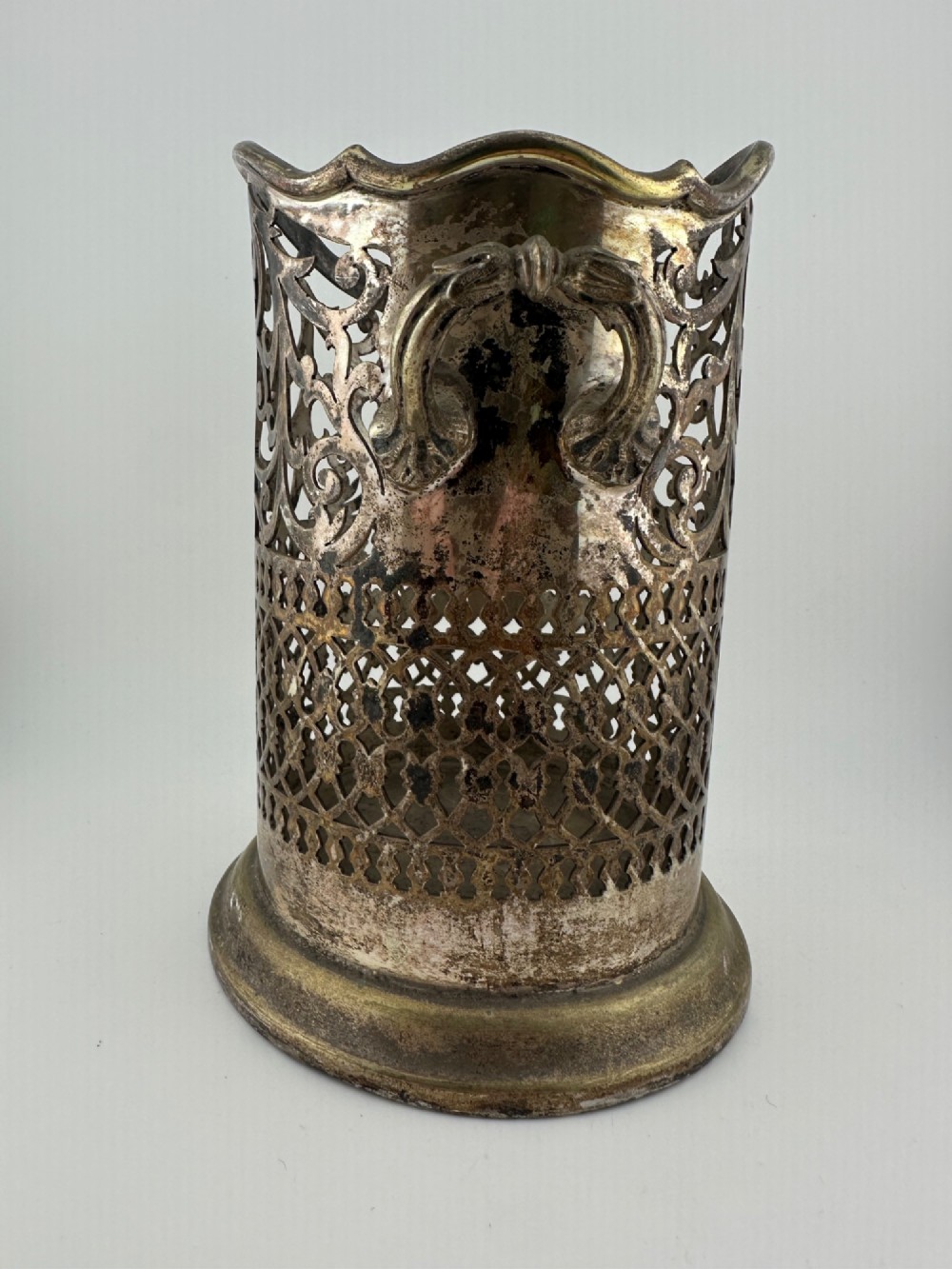 An antique silver-plated cylindrical wine bottle holder featuring pierced scroll fretwork, two side handles, and a flared circular base. View II