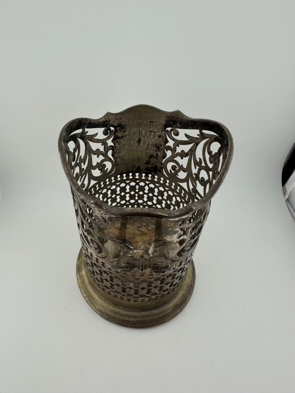 An antique silver-plated cylindrical wine bottle holder featuring pierced scroll fretwork, two side handles, and a flared circular base. View V