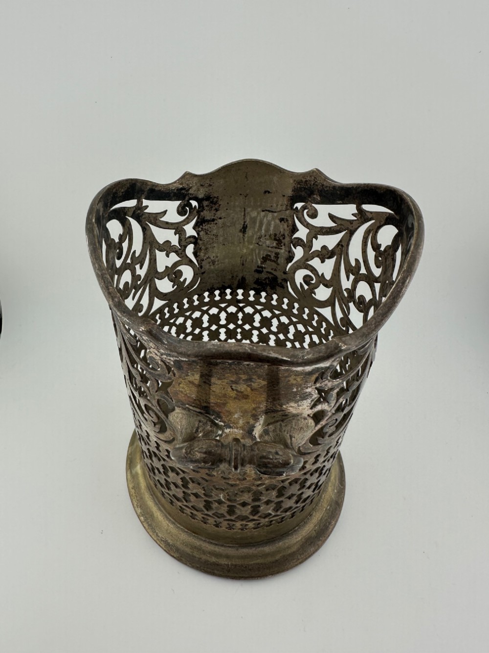 An antique silver-plated cylindrical wine bottle holder featuring pierced scroll fretwork, two side handles, and a flared circular base. View VI