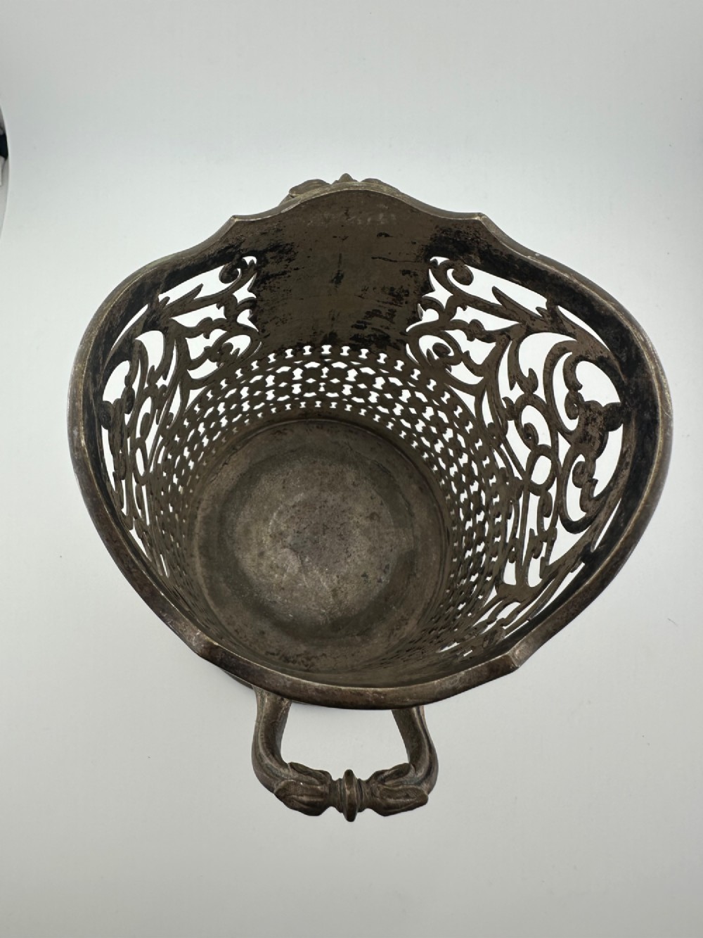 An antique silver-plated cylindrical wine bottle holder featuring pierced scroll fretwork, two side handles, and a flared circular base. View VII