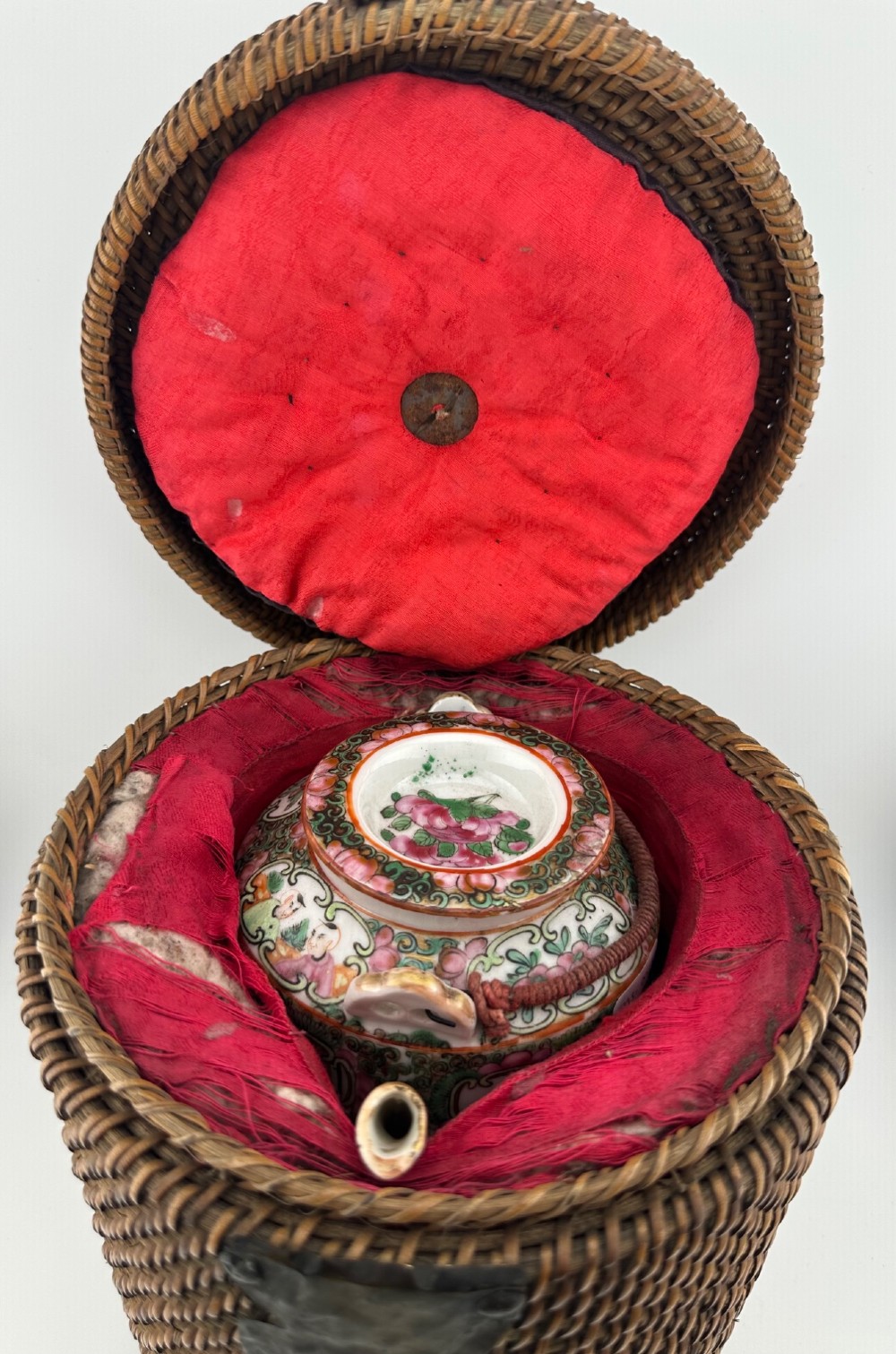 A Chinese Famille Rose cylindrical ceramic teapot with hand-painted court figures set beside its fitted woven wicker carrying case. View III
