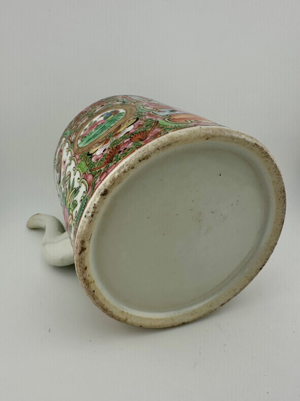 A Chinese Famille Rose cylindrical ceramic teapot with hand-painted court figures set beside its fitted woven wicker carrying case. View V