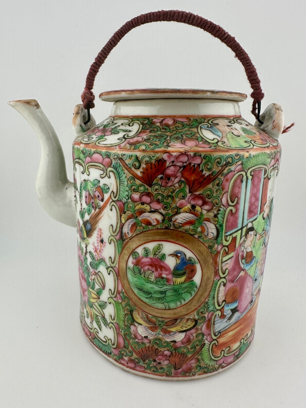 A Chinese Famille Rose cylindrical ceramic teapot with hand-painted court figures set beside its fitted woven wicker carrying case. View VI