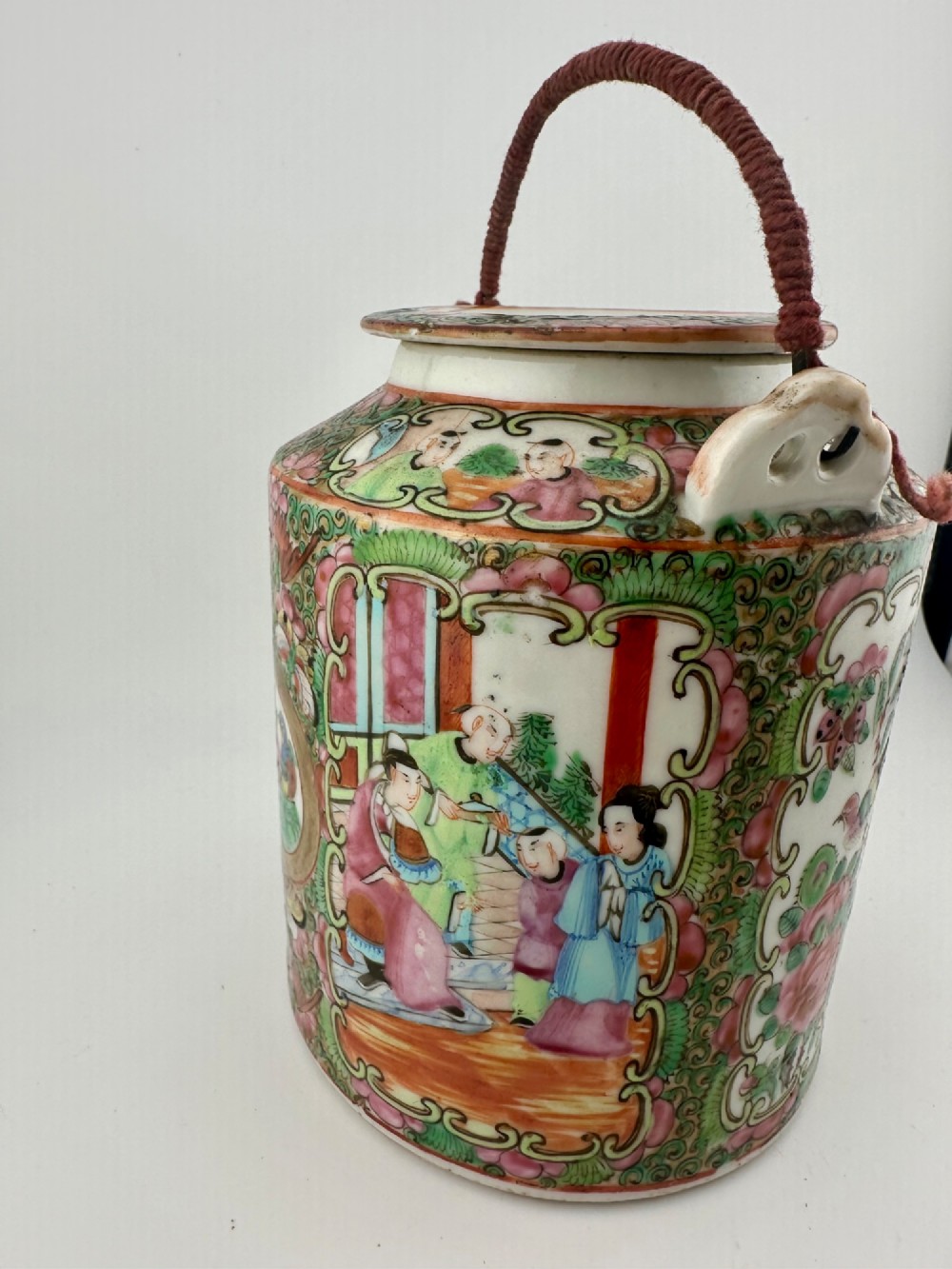 A Chinese Famille Rose cylindrical ceramic teapot with hand-painted court figures set beside its fitted woven wicker carrying case. View VII