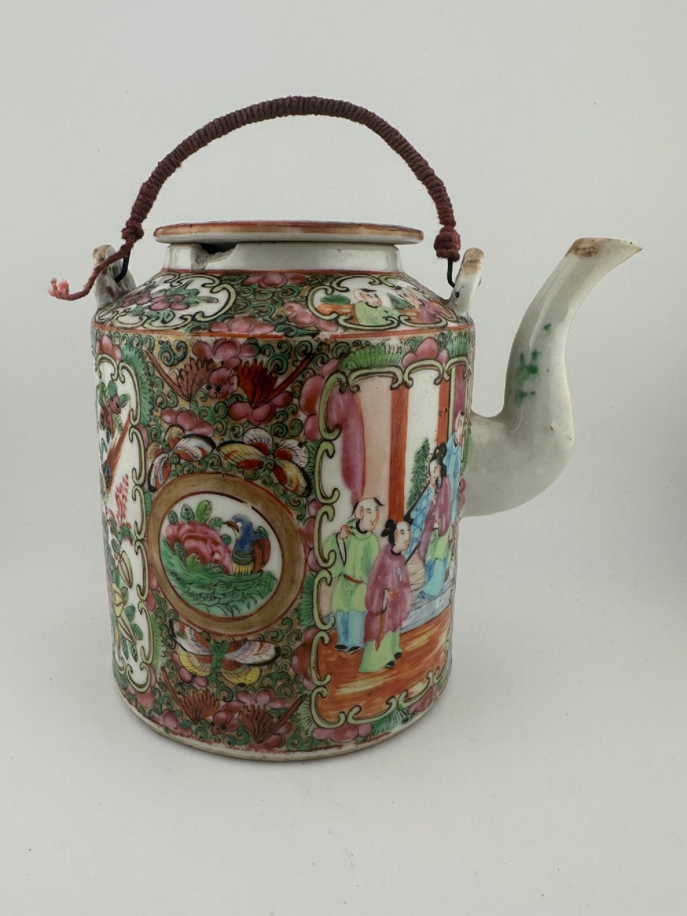 A Chinese Famille Rose cylindrical ceramic teapot with hand-painted court figures set beside its fitted woven wicker carrying case. View VIII
